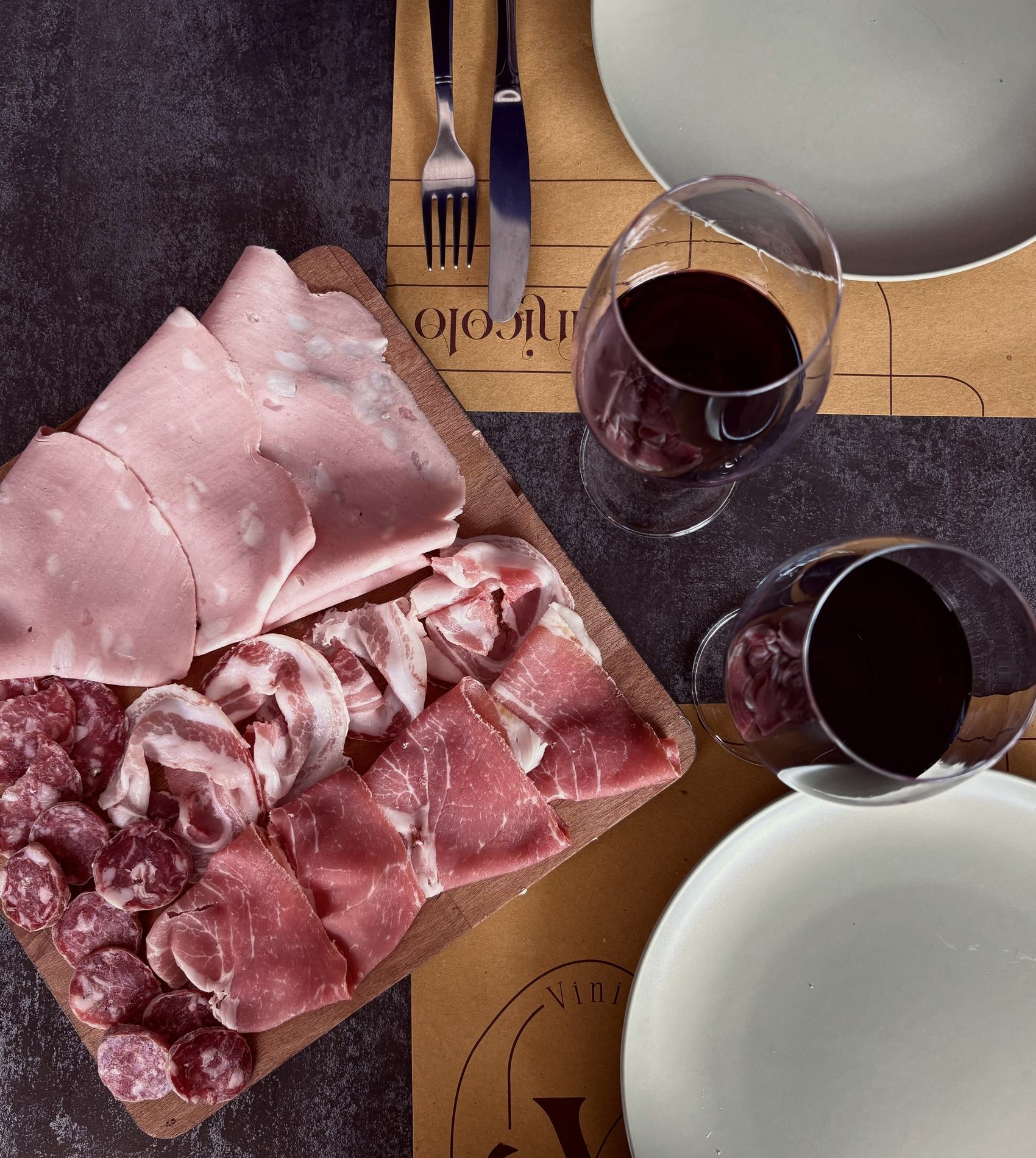 Tagliere di salumi e due calici di rosso sul tavolo di Vinicolo